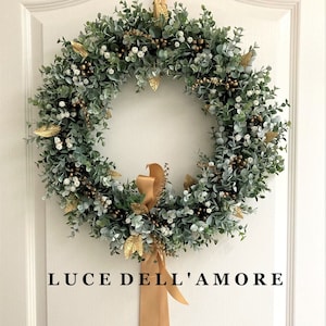 May include: A green eucalyptus wreath with gold accents and white berries, decorated with a gold ribbon and the text "LUCE DELL'AMORE".