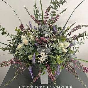 May include: A bouquet of purple, white, and green flowers in a gray box with the text "LUCE DELL'AMORE" on the front.