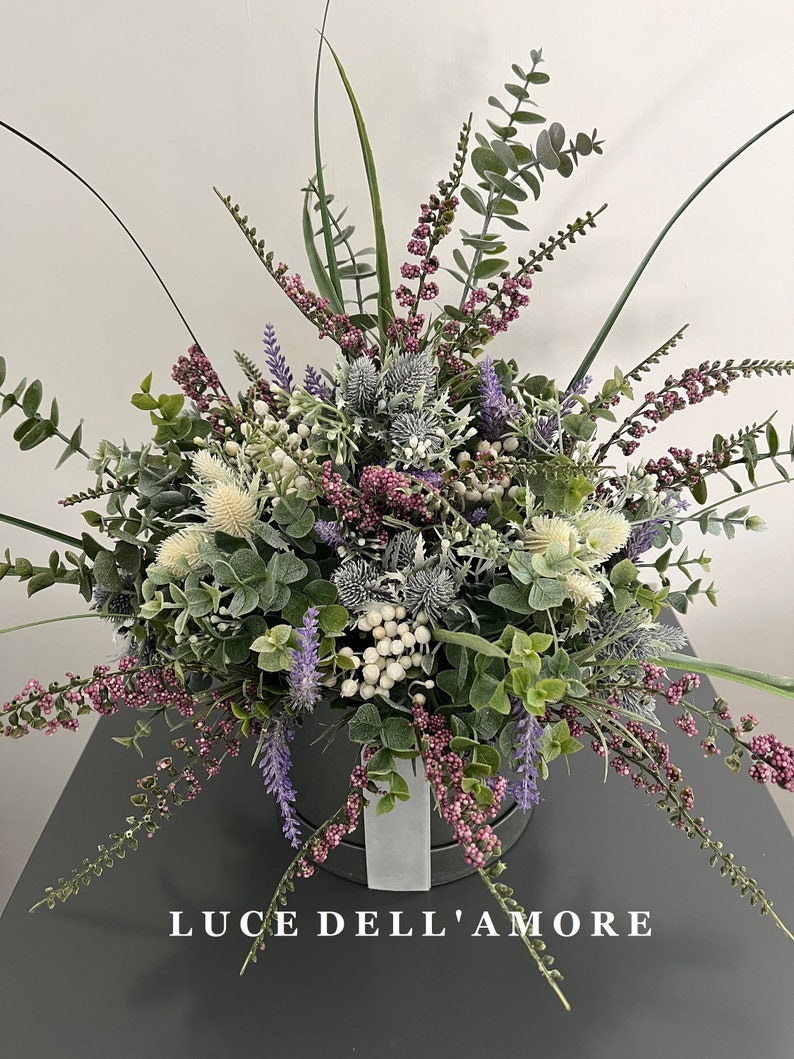 May include: A bouquet of purple, white, and green flowers in a gray box with the text "LUCE DELL'AMORE" on the front.