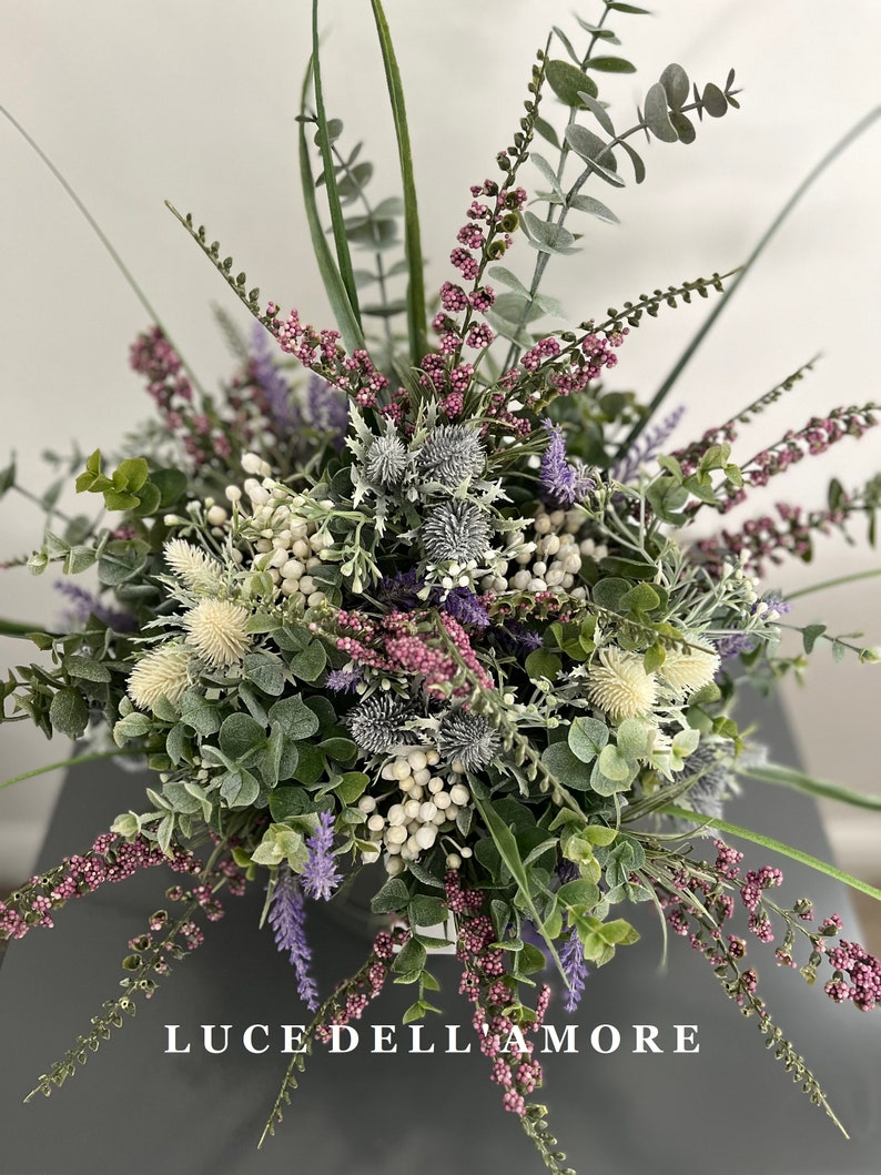 May include: A bouquet of artificial flowers in shades of purple, white, and green. The bouquet includes sprigs of lavender, eucalyptus, and thistle. The text "LUCE DELL'AMORE" is visible at the bottom of the image.
