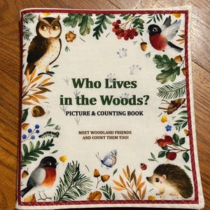 May include: A children's book titled "Who Lives in the Woods?" features illustrations of woodland creatures like an owl, birds, and a hedgehog. The cover is bordered with a red stitched edge and includes the text "Picture & Counting Book."