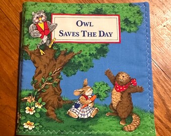 May include: A fabric book titled "Owl Saves The Day" with illustrations of an owl, a rabbit, and a beaver. The cover is blue with green trim and features a tree and flowers.