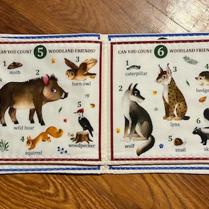 May include: A fabric book featuring woodland creatures. The left page displays a moth, wild boar, barn owl, squirrel, and woodpecker. The right page shows a caterpillar, wolf, lynx, hedgehog, snail, and skunk. Text reads "CAN YOU COUNT WOODLAND FRIENDS?"