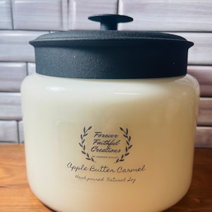Pode incluir: Uma vela de vidro branco em um frasco com uma tampa preta e um rótulo preto que diz "Forever Faithful Creations by Jennifer Whaley Apple Butter Caramel Hand poured Natural Soy".