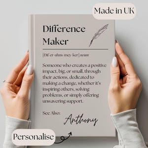 Könnte beinhalten: Ein beiges Buch mit dem Text "Difference Maker" in schwarzer Schrift. Das Buch enthält eine Definition des Wortes "Difference Maker" und das Wort "Anthony" steht unten in Kursivschrift. Das Buch wird von den Händen einer Person gehalten. Der Text "Personalisieren" ist in schwarzer Schrift auf einem weißen Kreis mit einem Pfeil, der auf das Buch zeigt, geschrieben.