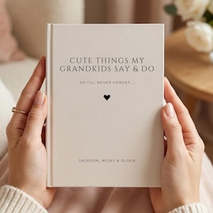May include: A cream-colored hardcover journal with black text that reads CUTE THINGS MY GRANDKIDS SAY & DO, SO I'LL NEVER FORGET..., a small black heart icon, and the names JACKSON, NICKY & OLSEN printed at the bottom of the front cover.