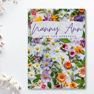 May include: A greeting card with the text "Nanny Ann I miss you everyday" in a white banner. The card is covered in colorful flowers, including daisies, roses, and other blooms. The background is white.