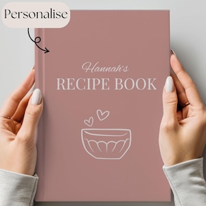 May include: A pink recipe book with the text "Hannah's RECIPE BOOK" and a white outline of a mixing bowl with hearts above it.