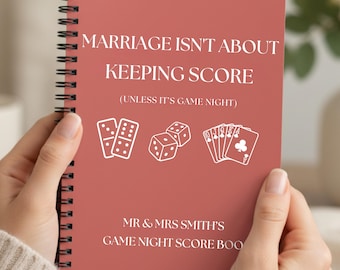 May include: A spiral-bound notebook with a terracotta cover featuring white text that reads: MARRIAGE ISN'T ABOUT KEEPING SCORE (UNLESS IT'S GAME NIGHT) MR & MRS SMITH'S GAME NIGHT SCORE BOOK, accompanied by white line art of dominoes, dice, and playing cards.