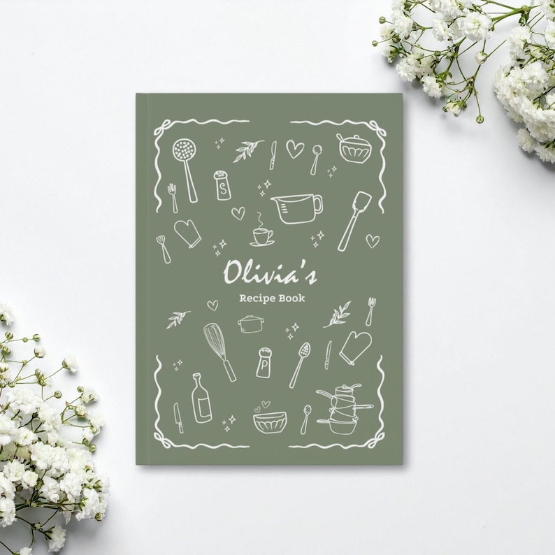 Puede incluir: Un libro de recetas verde salvia con el t&iacute;tulo "Olivia's Recipe Book" en una fuente manuscrita. La portada presenta dibujos lineales blancos de utensilios de cocina y alimentos, incluyendo un batidor, una cuchara y una taza medidora.