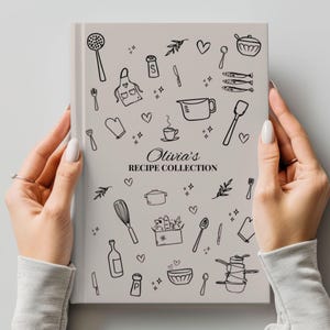 Pode incluir: Um livro de receitas cinza claro intitulado "Olivia's Recipe Collection" segurado por mãos. A capa apresenta desenhos a traço preto de utensílios de cozinha, alimentos e corações. O livro é retangular e tem um design limpo e minimalista.