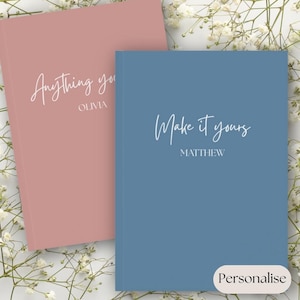 Peut inclure: Deux journaux à couverture rigide, un rose poudré et un bleu, avec du texte en écriture blanche. Le journal rose poudré indique "Anything you" avec "Olivia" en dessous. Le journal bleu indique "Make it yours" avec "Matthew" en dessous. Le mot "Personalise" est en bas à droite.