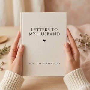 以下が含まれることがあります： 表紙に黒い文字で「LETTERS TO MY HUSBAND」と印刷されたクリーム色のハードカバーブック。タイトルの下には小さな黒いハートのアイコンがあり、下端近くには「WITH LOVE ALWAYS, SUE X」というテキストが印刷されています。