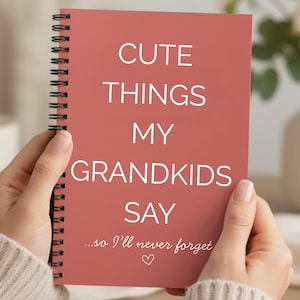 May include: A spiral-bound notebook with a dusty rose cover held by two hands. The cover features the text "CUTE THINGS MY GRANDKIDS SAY" in white, with the phrase "...so I'll never forget" and a heart symbol below.