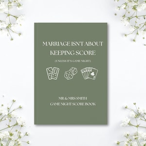 May include: A sage green score book with white text that reads MARRIAGE ISN'T ABOUT KEEPING SCORE (UNLESS IT'S GAME NIGHT) followed by MR & MRS SMITH GAME NIGHT SCORE BOOK. The cover features white line art of dominoes, dice, and playing cards.