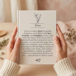 Könnte beinhalten: Ein Hardcover-Buch mit dem Namen "Emma" und der Zahl "40" auf dem Einband. Die Seiten des Buches enthalten Text über die Kapitel des Lebens, Liebe, Lektionen und Lachen. Über dem Namen befindet sich ein Blumendesign.
