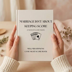 May include: A cream-colored hardcover book titled MARRIAGE ISN'T ABOUT KEEPING SCORE (UNLESS IT'S GAME NIGHT) with a graphic of five playing cards showing a royal flush in clubs, and the text MR & MRS SIMMONS GAME NIGHT SCORE BOOK printed below.