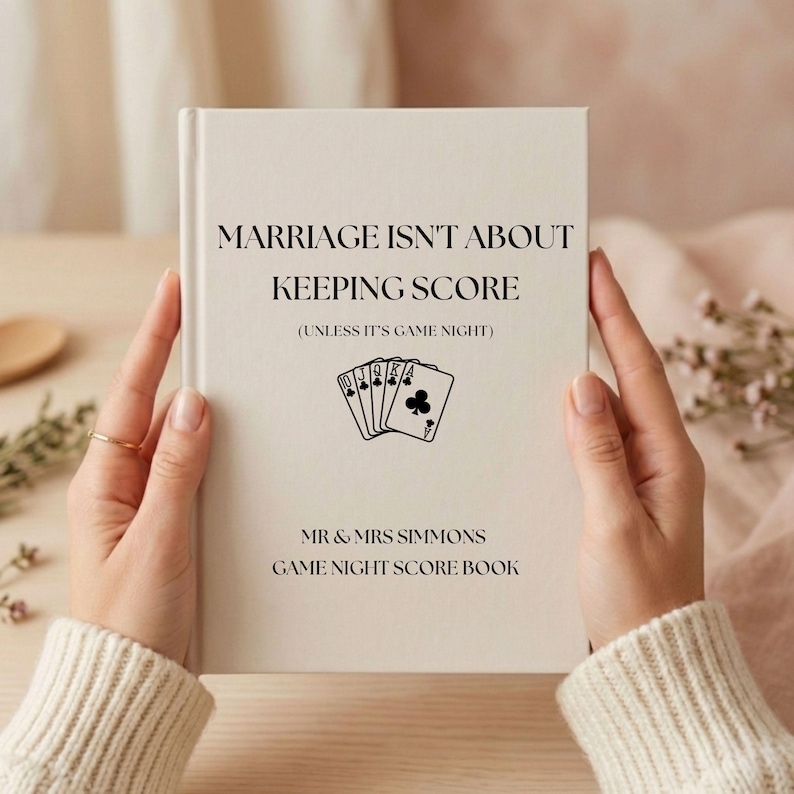 May include: A cream-colored hardcover book titled MARRIAGE ISN'T ABOUT KEEPING SCORE (UNLESS IT'S GAME NIGHT) with a graphic of five playing cards showing a royal flush in clubs, and the text MR & MRS SIMMONS GAME NIGHT SCORE BOOK printed below.