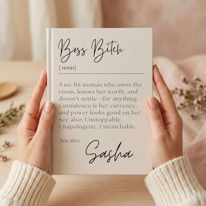May include: A white book with the words "Boss Bitch" in elegant script. The text defines a confident woman who knows her worth. The name "Sasha" is written at the bottom. The book is held by a person.