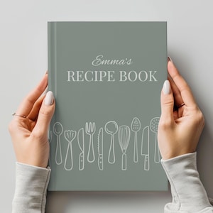 May include: A sage green hardback book with the white text Emma's RECIPE BOOK printed on the front cover. The lower portion of the cover features a white line art illustration of various kitchen utensils including spoons, a whisk, and knives.