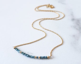 May include: A gold chain necklace with a delicate row of blue gemstone beads.
