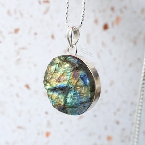 May include: A silver chain necklace with a round pendant featuring a green, blue and gold labradorite stone.