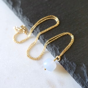 May include: A delicate gold chain necklace with a single, round, light blue gemstone pendant.