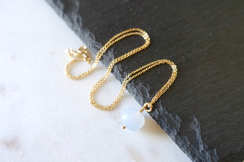 May include: A delicate gold chain necklace with a single, round, light blue gemstone pendant.