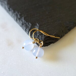 May include: A pair of delicate gold earrings with light blue round gemstone beads.