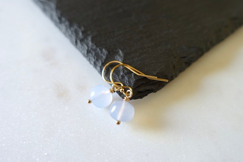 May include: A pair of delicate gold earrings with light blue round gemstone beads.
