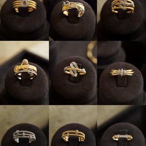 Pu&ograve; includere: Nove anelli in oro e argento con accenti di diamanti esposti su cuscini di velluto nero. Gli anelli presentano vari design, tra cui un cerchio, un nodo e una linea retta.