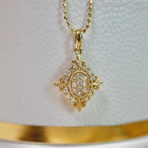 Può includere: Una collana con un ciondolo in oro a forma di diamante con un gruppo di piccoli diamanti. Il ciondolo è ornato e presenta un design delicato e intricato.
