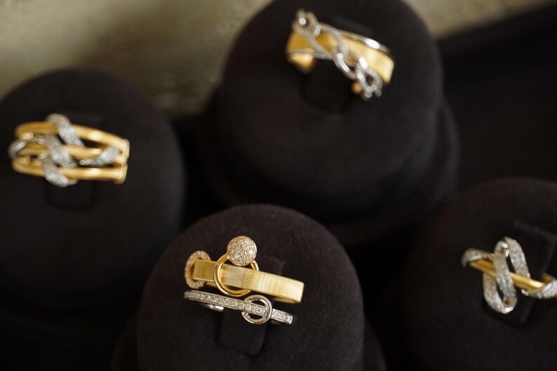 Pu&ograve; includere: Quattro anelli d'oro con accenti di diamanti esposti su cuscini di velluto nero. Gli anelli sono di stili diversi, tra cui una fascia attorcigliata, un anello con una pietra rotonda e un anello con un design a catena delicato.