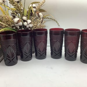 Könnte beinhalten: Ein Set aus sechs dunkelroten Glastrinkbechern mit einem strukturierten Rautenmuster im oberen Bereich und einem gepressten Blattdesign im unteren Teil. Jeder zylindrische Becher hat einen glatten Rand und eine durchgehend dunkle Rubinrotfärbung.