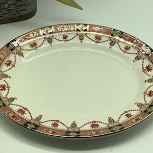 May include: An oval serving dish with a white center and a decorative border. The border features a repeating pattern of gold, red, blue, and green floral motifs.