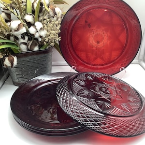 May include: A set of three deep red glass plates featuring a pressed pattern with a central starburst design surrounded by a diamond-cut border. The plates are translucent, showing a geometric texture on the underside and a smooth surface on top.