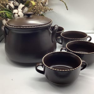 Peut inclure: Un service à soupe en céramique marron foncé comprenant une soupière avec couvercle et deux anses, ainsi que quatre bols assortis. Chaque bol et le couvercle de la soupière sont ornés d'une bordure blanche décorative.