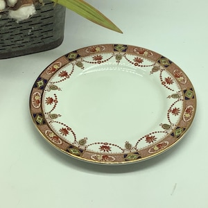 May include: A white porcelain plate with a gold, red, and blue floral pattern around the rim.