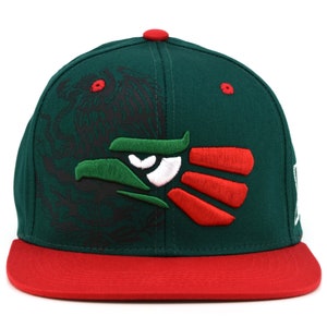 Puede incluir: Una gorra de b&eacute;isbol verde y roja con un dise&ntilde;o de &aacute;guila bordado. El &aacute;guila tiene la cabeza verde, los ojos blancos y las alas rojas. La gorra tiene una visera roja.