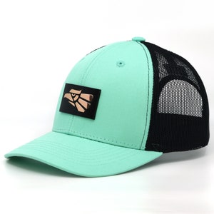 Peut inclure: Un chapeau de camionneur vert menthe et noir avec un emblème d'aigle doré sur le devant. Le chapeau a un dos en maille.