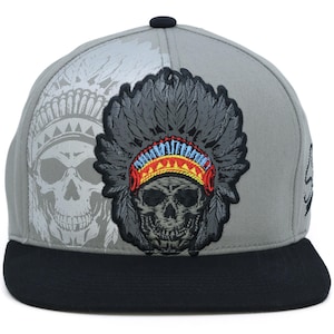 Puede incluir: Gorra de béisbol gris con visera negra y diseño de calavera. La gorra presenta una calavera bordada detallada con un tocado nativo americano. Un gráfico de calavera descolorido está en el lateral.