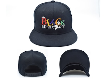 May include: Black baseball cap with an embroidered design that reads "I Am Black History" in rainbow colors with a black fist and an outline of Africa.