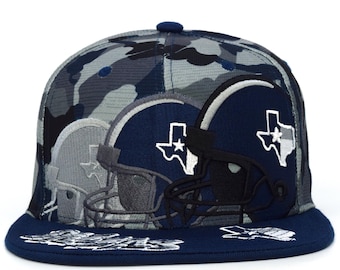 Op de afbeelding: Een marineblauwe en camouflage baseballcap met meerdere voetbalhelm-ontwerpen. De helmen zijn marineblauw en grijs met een witte Texas-ster. De pet heeft een platte klep en een knoop aan de bovenkant.