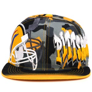 Op de afbeelding: Een zwarte en gele camouflage baseballcap met een wit en geel Pittsburgh Steelers logo op de voorkant. De cap heeft een zwarte klep met een gele onderkant.