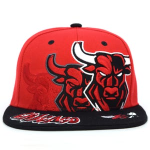 Könnte beinhalten: Rote Baseballkappe mit schwarzem Schirm, mit dem Logo der Chicago Bulls. Das Logo ist ein stilisierter Bulle in Rot, Schwarz und Weiß. Die Kappe hat eine rote Krone.