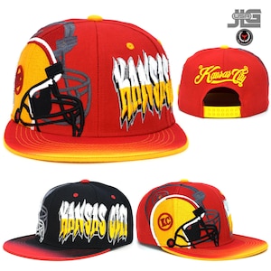 May include: Three red, black, and yellow baseball caps with the words "Kansas City" and a football helmet graphic. The caps have a curved brim and a mesh back.