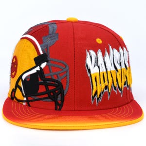 May include: Red and yellow baseball cap with a football helmet graphic and the word "KANSAS" in a stylized font.