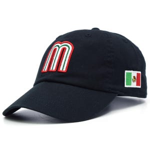 Puede incluir: Gorra de béisbol negra con una 'M' estilizada en rojo, blanco y verde, y un pequeño parche de la bandera mexicana. La gorra tiene una visera curva y un diseño clásico.