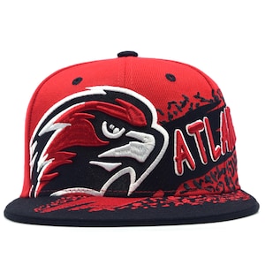 May include: A red and black baseball cap featuring an embroidered hawk head logo on the front panel. The word ATLANTA is stitched in red with a white outline on the side. The design includes a black speckled pattern across the crown and brim.