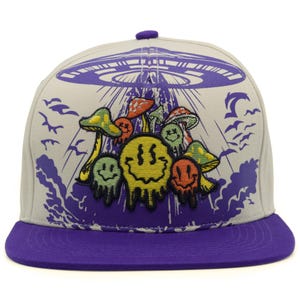 Puede incluir: Una gorra de béisbol gris claro con visera plana morada y un botón morado en la parte superior. El frente presenta un gráfico morado de un OVNI proyectando luz sobre un grupo de caras sonrientes que se derriten y setas bordadas.